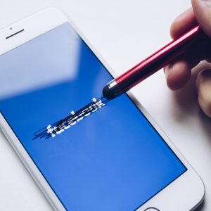 Close-up of a smartphone with a stylus crossing out text on its screen.