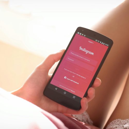 Woman holding a smartphone with Instagram login screen while relaxing indoors.