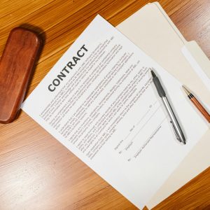 High-angle view of a contract document with pens and a case on a wooden table.