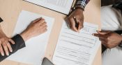 Close-up of two people signing documents at an office desk, depicting business collaboration.