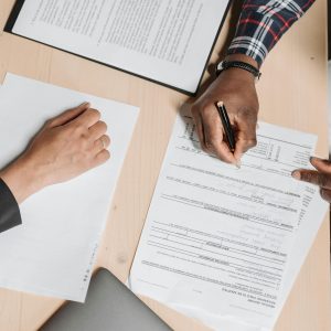 Close-up of two people signing documents at an office desk, depicting business collaboration.