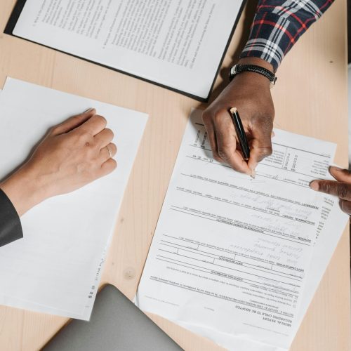 Close-up of two people signing documents at an office desk, depicting business collaboration.